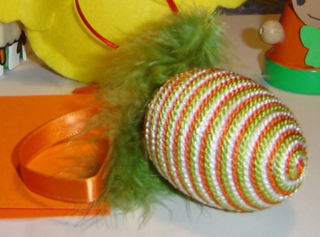 Plastično jajce ovito v 3 raznobarvne vrvice,okrašeno s svilenim trakom in perjem.