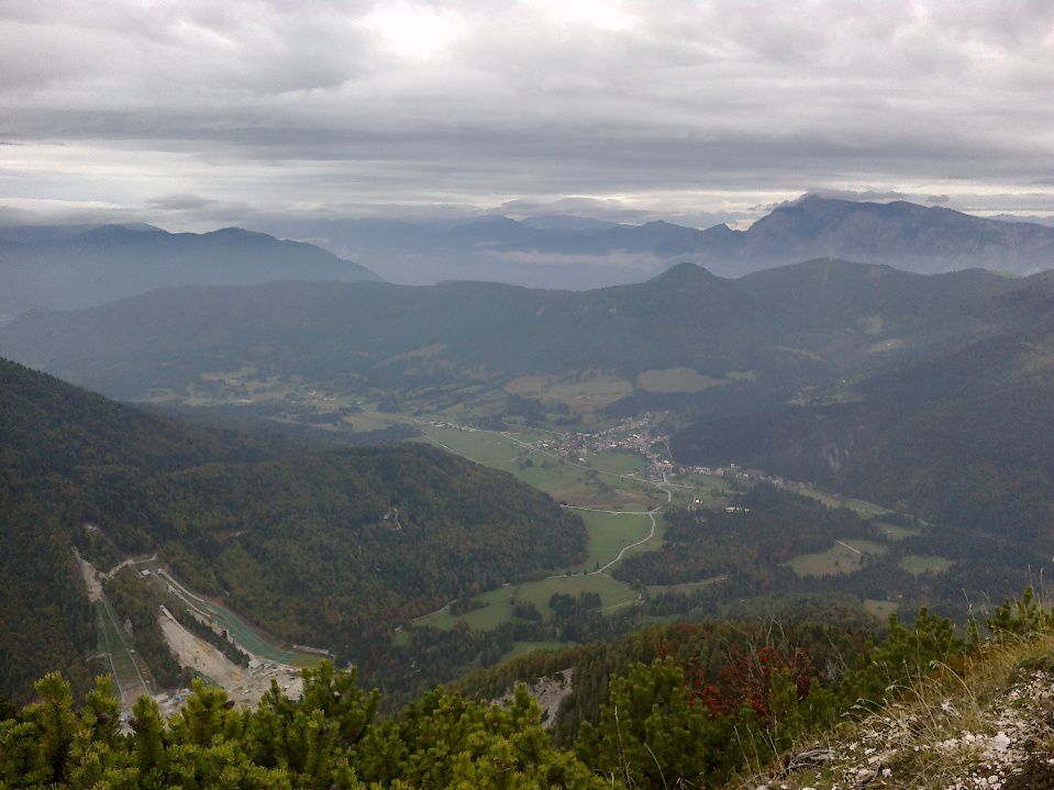 Pogled v dolino na smučarske skakalnice in Rateče ter Dobrač (v daljavi)