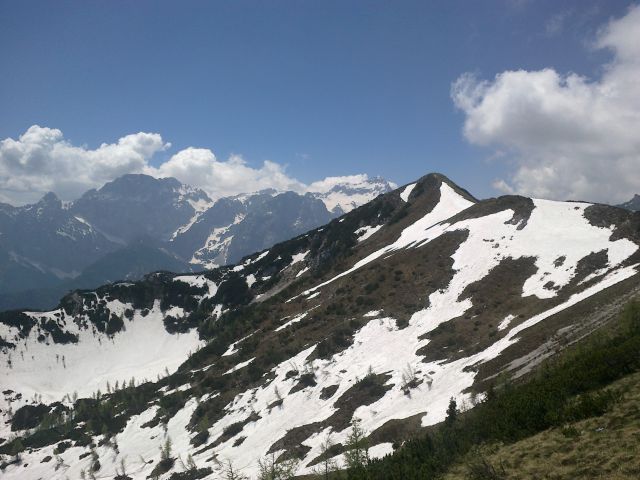 Razgled z vrha na Sleme (v ospredju) ter Rjavino (levo) in Triglav (desno) v ozadju